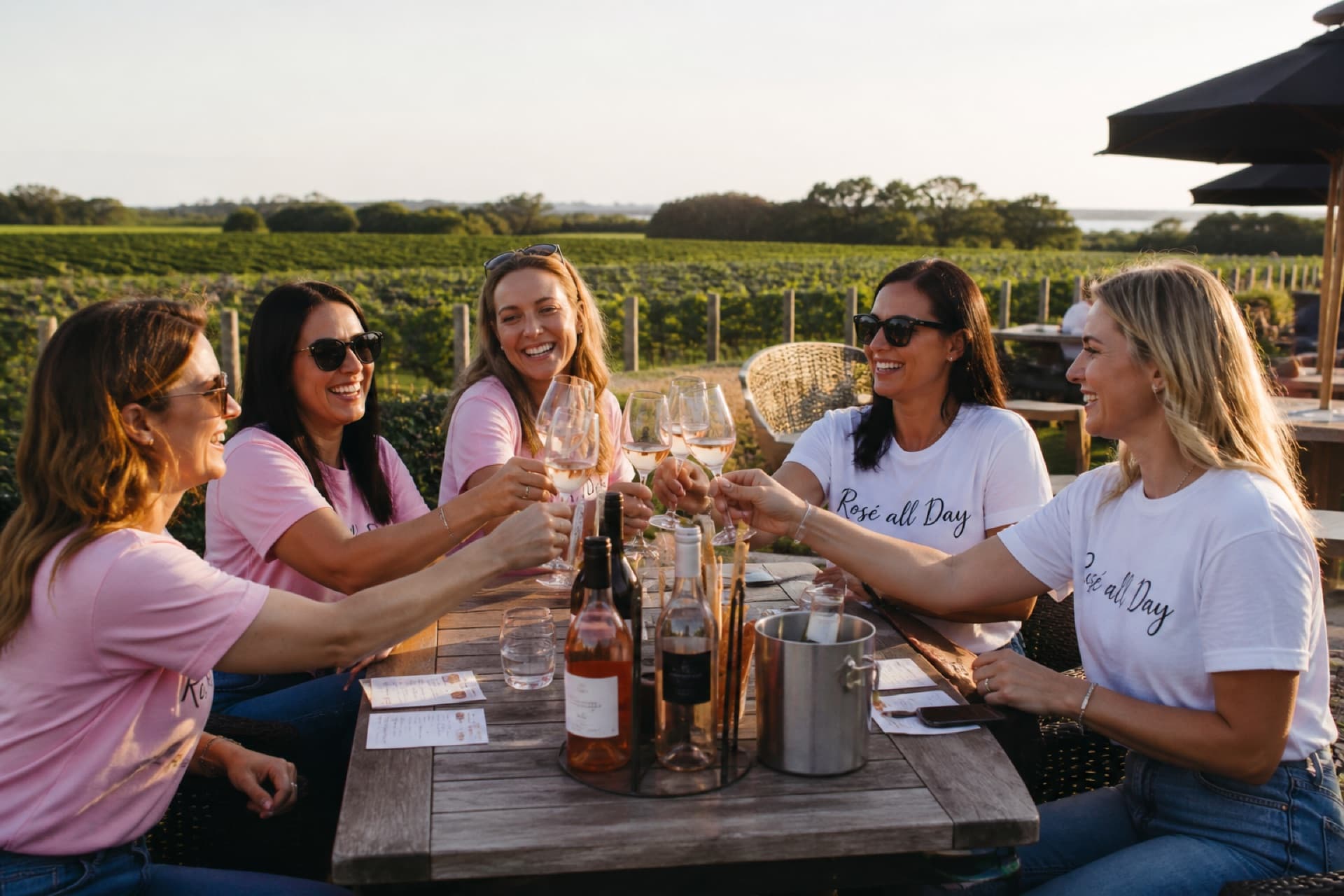 Group of women in matching outfits celebrating at an outdoor winery tasting table